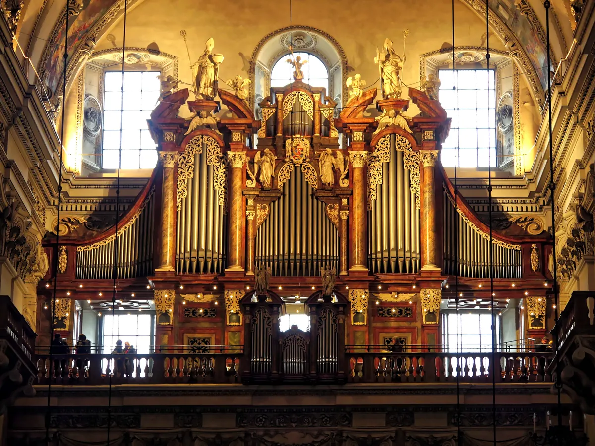 The great organ on the west gallery of Salzburg Cathedral, a tall case with gilded carving, carved figures on top and silver pipes in warm light