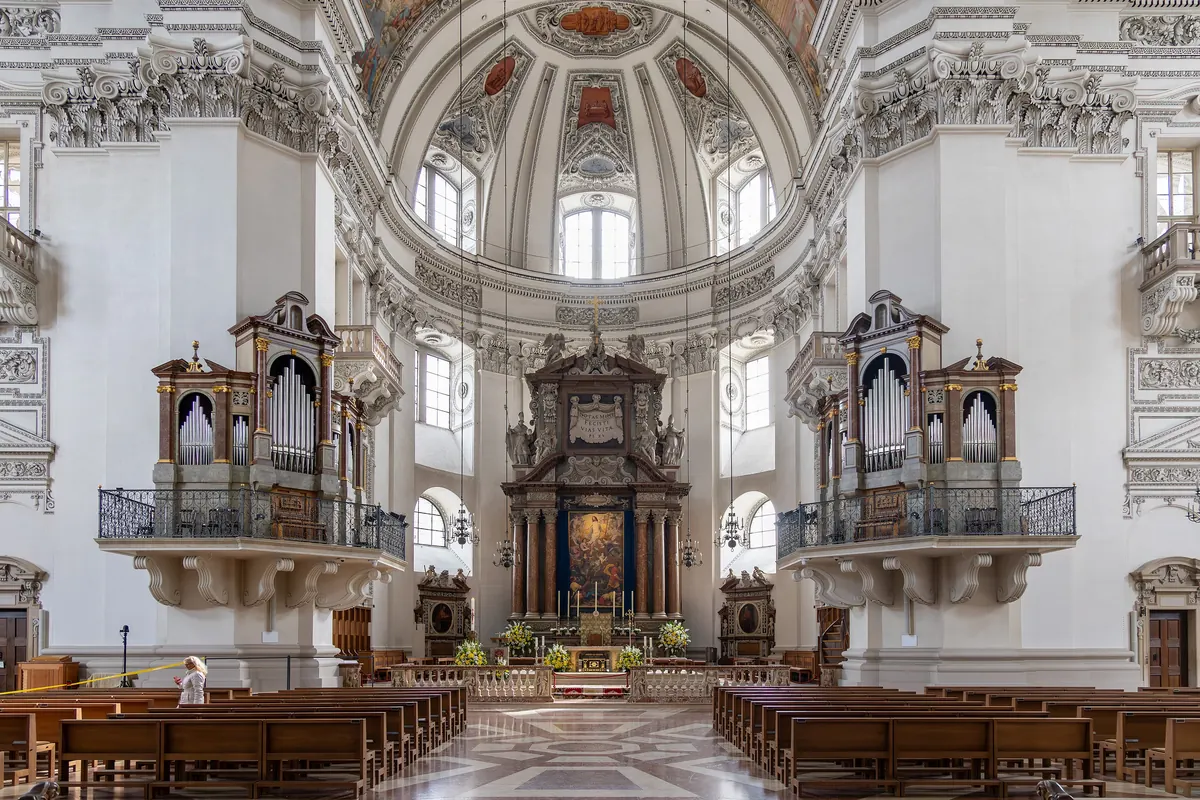 The nave of Salzburg Cathedral looking towards the altar, with a balcony organ on each of the two front pillars under the dome and rows of wooden pews below